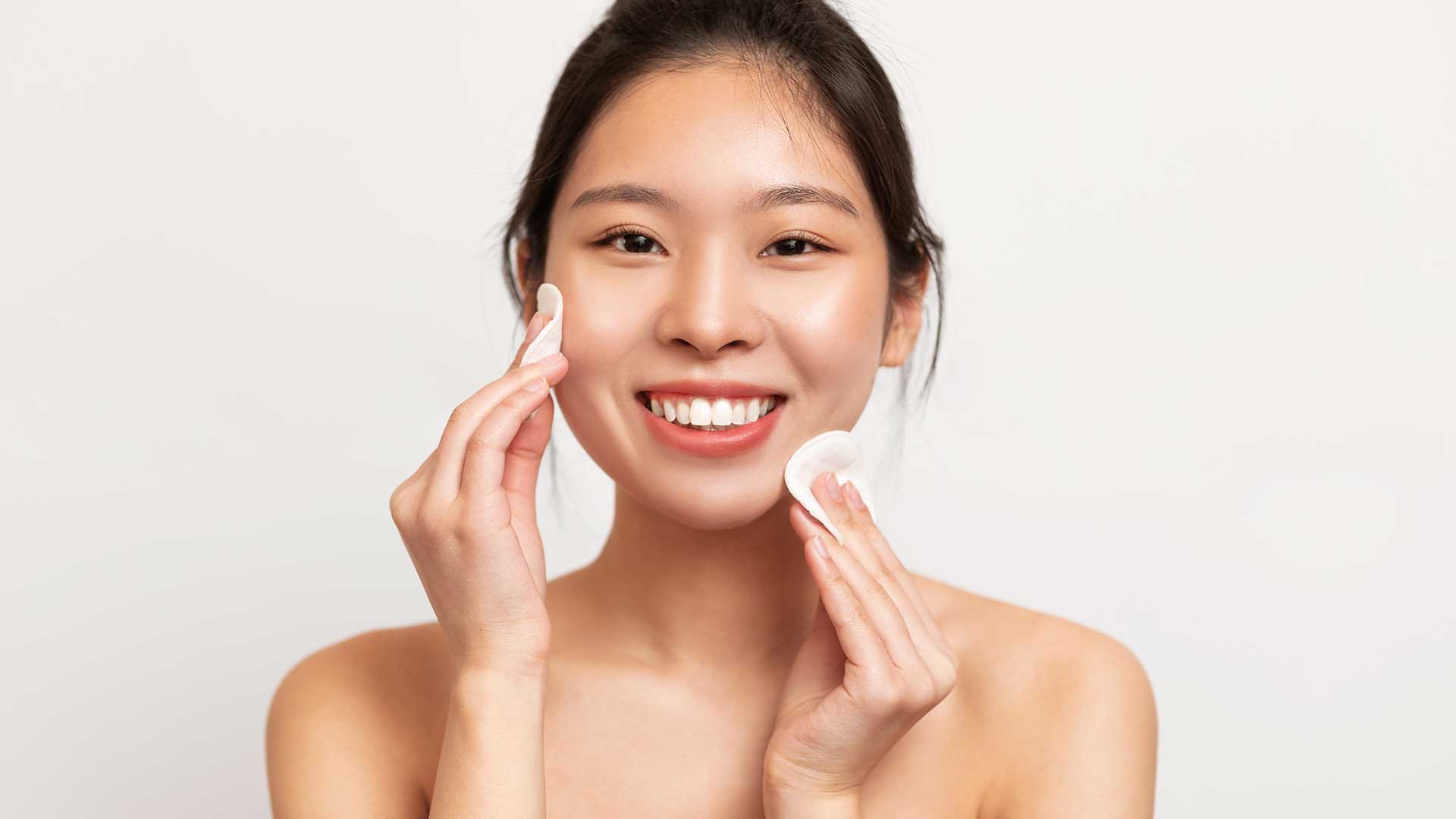 Junge Frau nutzt zwei Pads zur Reinigung ihrer Gesichtshaut