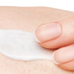 Une crème est appliquée avec deux doigts sur la main droite.