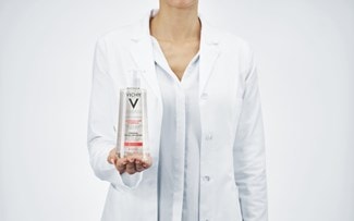 Frau in weissem Kittel hält das PURETÉ THERMALE Mizellenreinigungsfluid für empfindliche Haut 400 ml auf der Handfläche