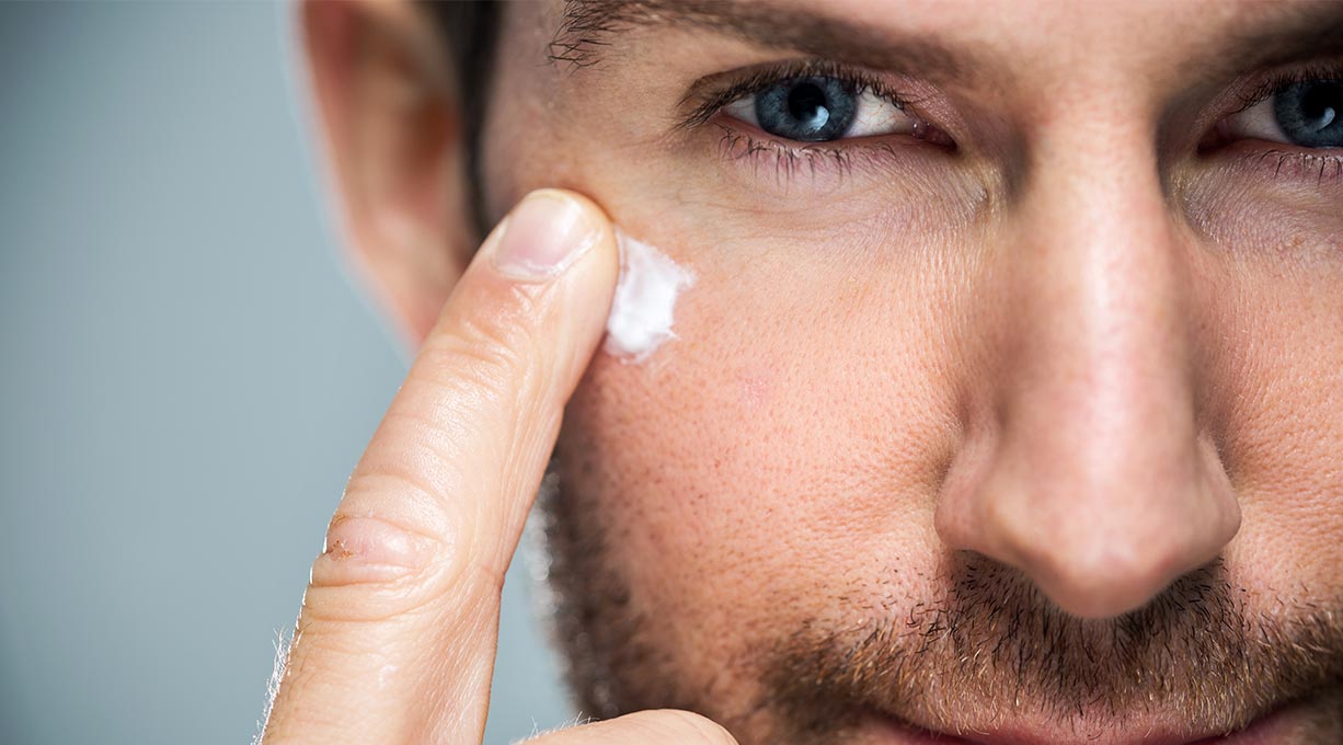 Gros plan sur le visage d'un homme avec une barbe. Il applique une crème pour visage sur sa joue droite avec son index.