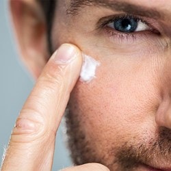 Mann mit Bart verstreicht eine kleine Menge weisser Creme auf seiner Wange