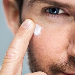 Gros plan sur le visage d'un homme avec une barbe. Il applique une crème pour visage sur sa joue droite avec son index.
