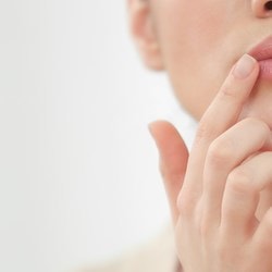 Untere Gesichtspartie einer Frau mit glatter Haut, die mit dem Zeigefinger ihren Mundwinkel berührt