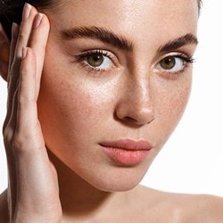 Gesicht einer jungen Frau mit glatter Haut, die sich zart mit der Hand an die Schläfen fasst