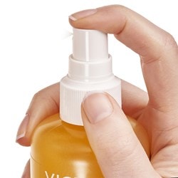 Hand hält ein Produkt mit einem Sprühkopf, der vom Zeigefinger nach unten gedrückt wird
