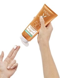 Une main de femme presse une noisette de crème solaire Vichy CAPITAL SOLEIL sur les doigts de son autre main