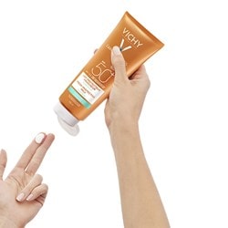 Eine Hand entnimmt eine kleine Menge Sonnencreme aus der CAPITAL SOLEIL Familienmilch von Vichy