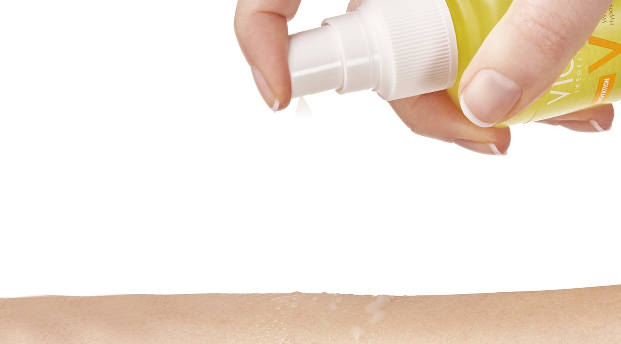 Detailbild von Sonnenspray, das über einen Sprühkopf auf die Haut gegeben wird