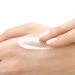 Weisse Creme mit von zwei Fingern mit gepflegten Nägeln auf der Haut verteilt